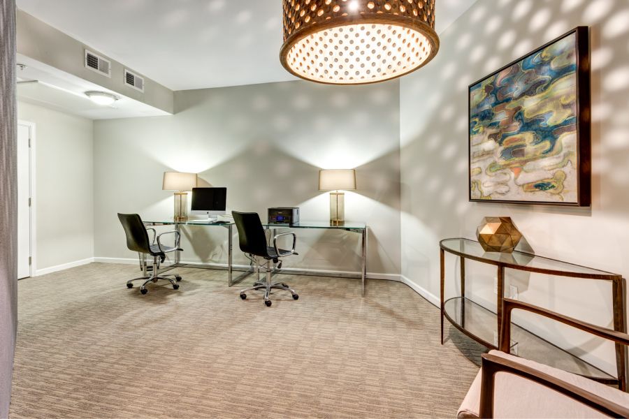 Modern office with two desks, black chairs, lamps, abstract wall art, and a round hanging light fixture.
