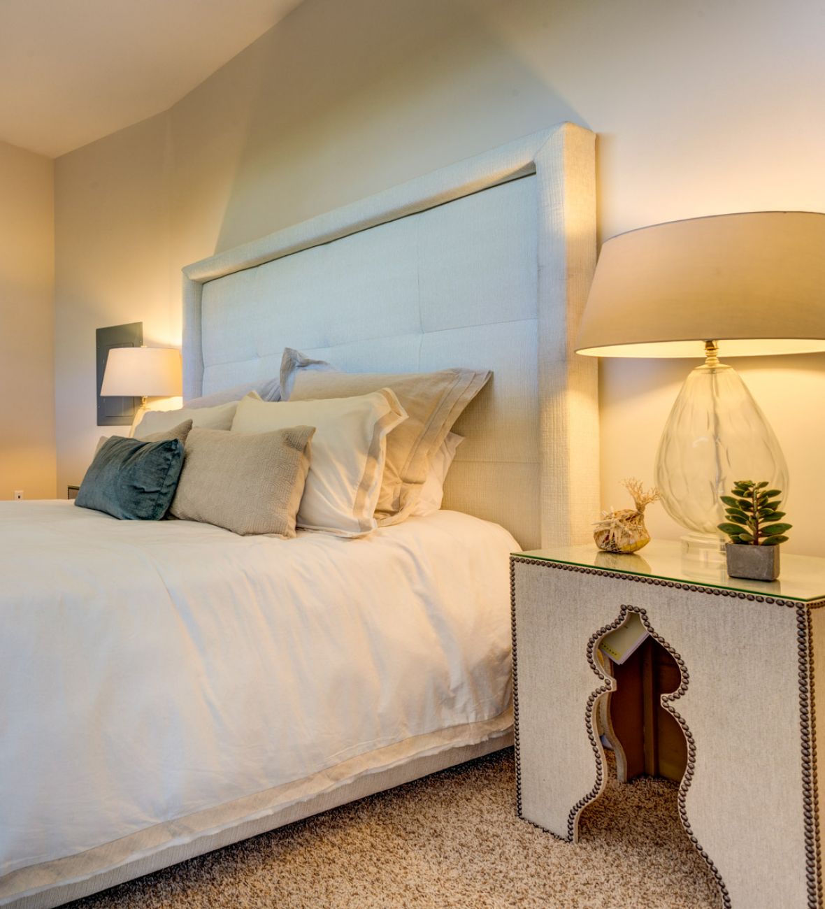 A cozy bedroom with a neatly made bed, two nightstands, a lamp, and a dresser with a sailboat picture.