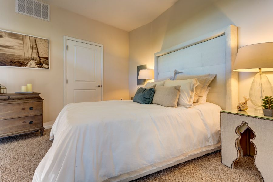 A cozy bedroom with a neatly made bed, two nightstands, a lamp, and a dresser with a sailboat picture.