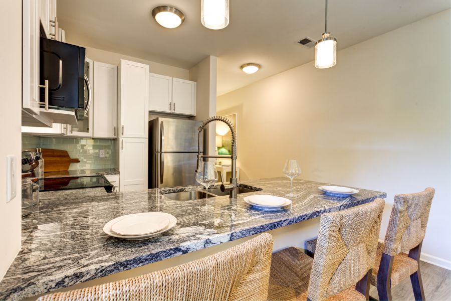 Modern kitchen with marble island, wicker bar stools, and stainless steel appliances, set with plates and glasses.