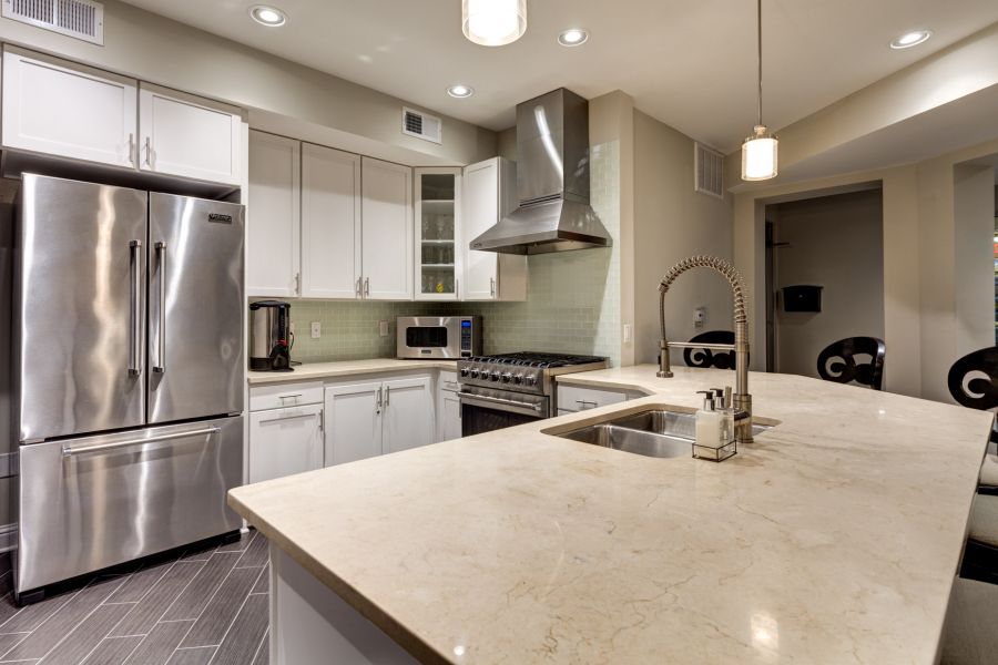 Modern kitchen with stainless steel appliances, white cabinets, and a marble island with a sink and faucet.