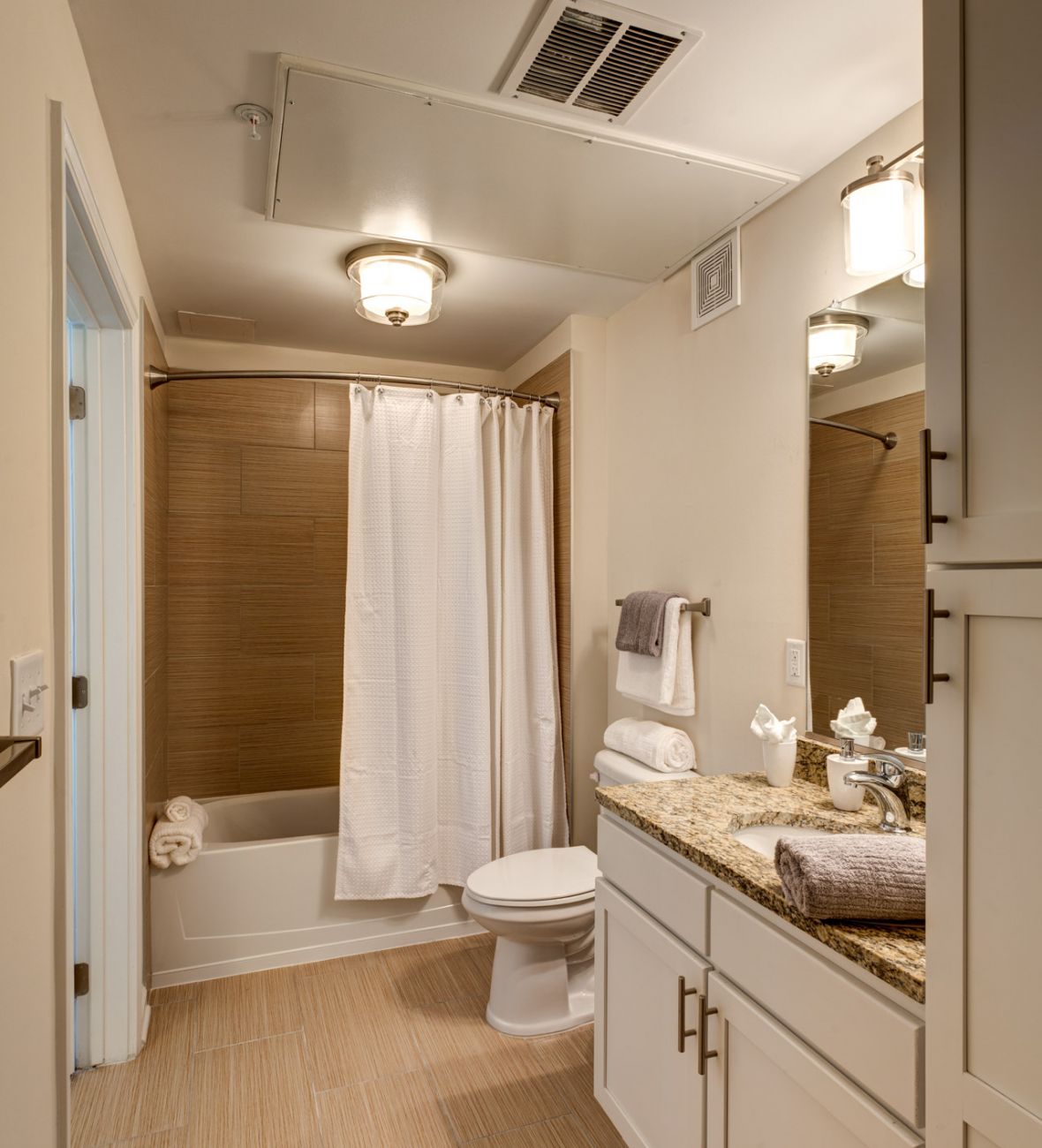 Modern bathroom with a granite countertop, white cabinets, bathtub with shower, and beige tile floor.