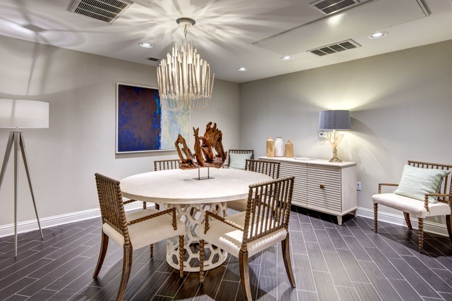 Modern dining room with round table, wicker chairs, chandelier, sideboard, and contemporary decor.