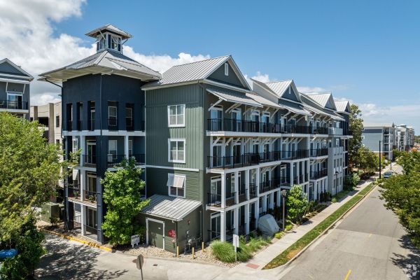 Modern multi-story apartment building with balconies and a metal roof on a sunny day.