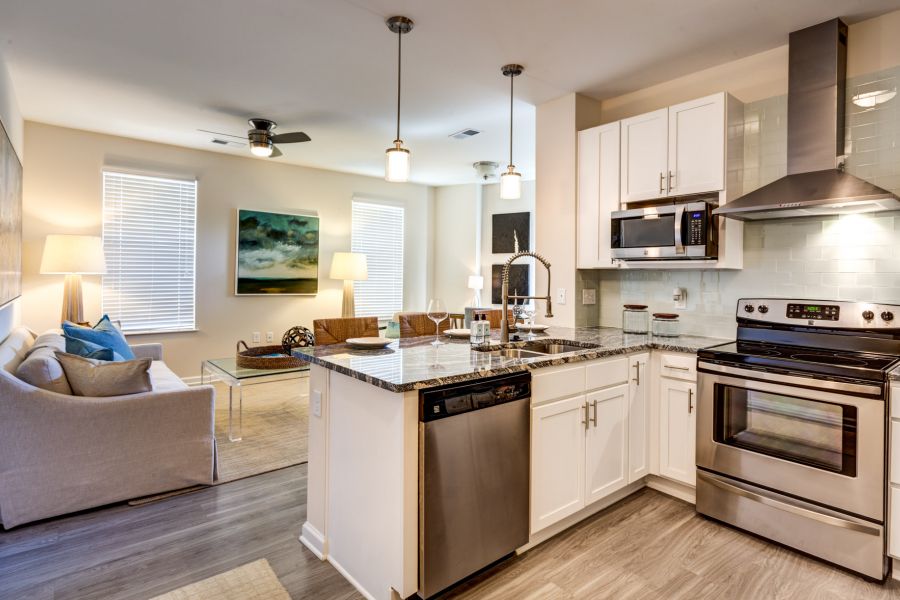 Modern kitchen with white cabinets, stainless steel appliances, and open living room with sofa and artwork.