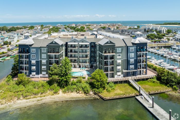 A large waterfront apartment complex with balconies, near a marina and surrounded by water and greenery.