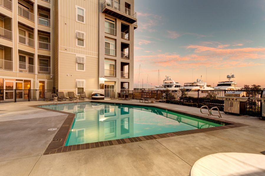 Outdoor pool beside an apartment building with yachts and a sunset sky in the background.