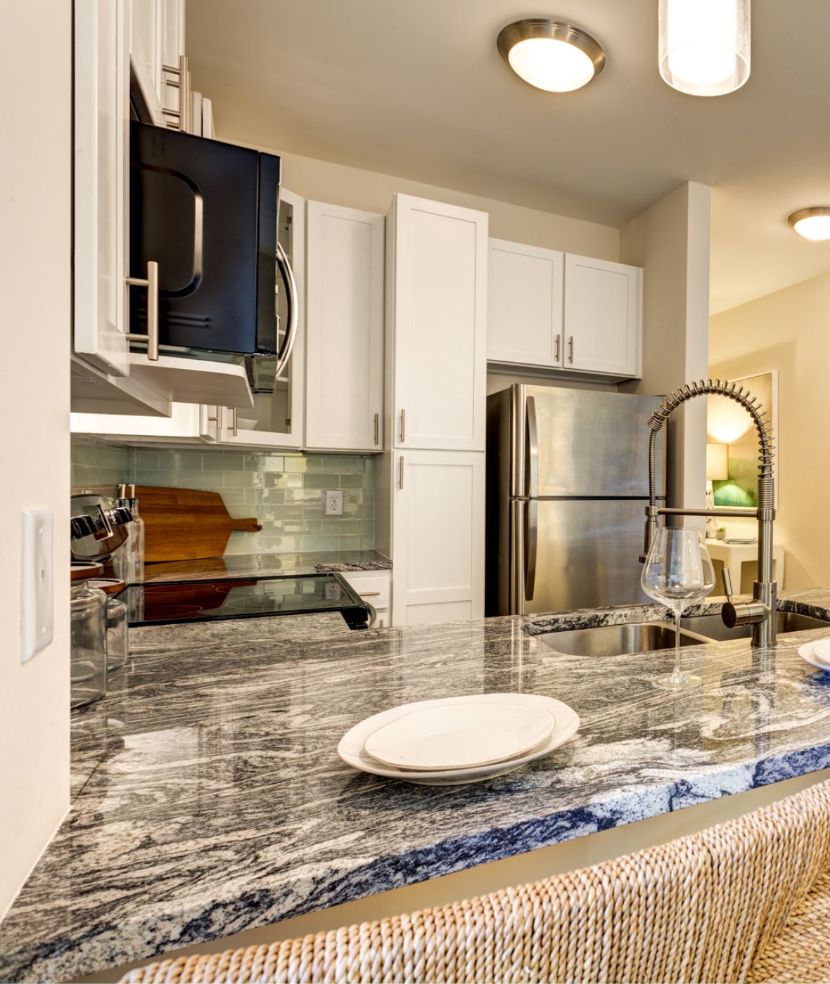 Modern kitchen with marble island, wicker bar stools, and stainless steel appliances, set with plates and glasses.