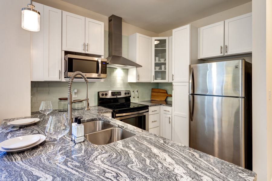 Modern kitchen with white cabinets, stainless steel appliances, and a gray marble countertop with place settings.