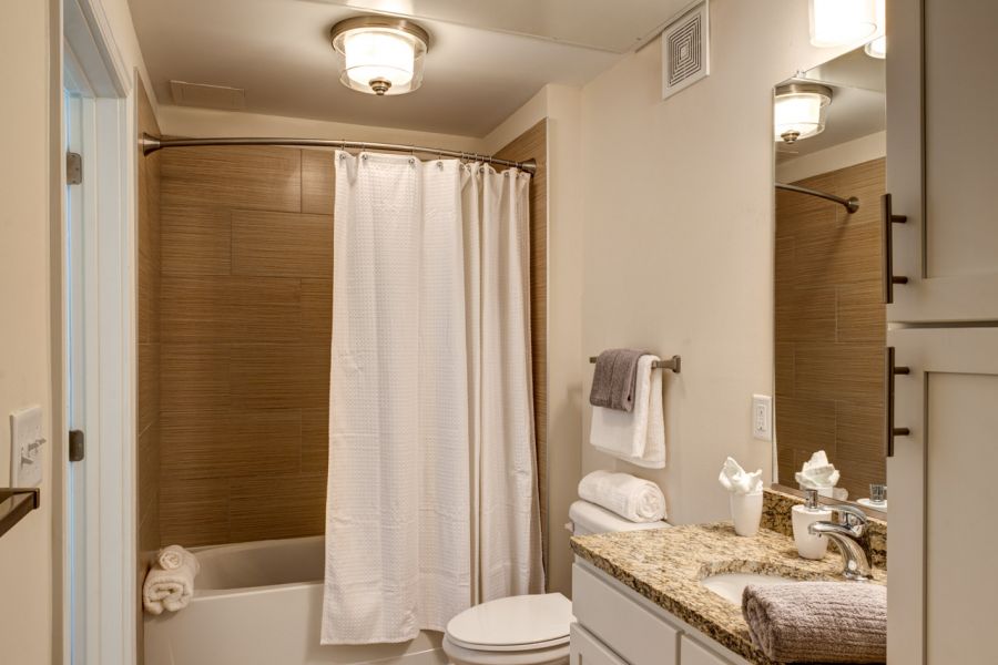 Modern bathroom with a granite countertop, white cabinets, bathtub with shower, and beige tile floor.