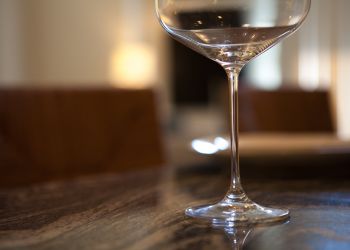 A close-up of an empty wine glass on a polished table with a blurred background.