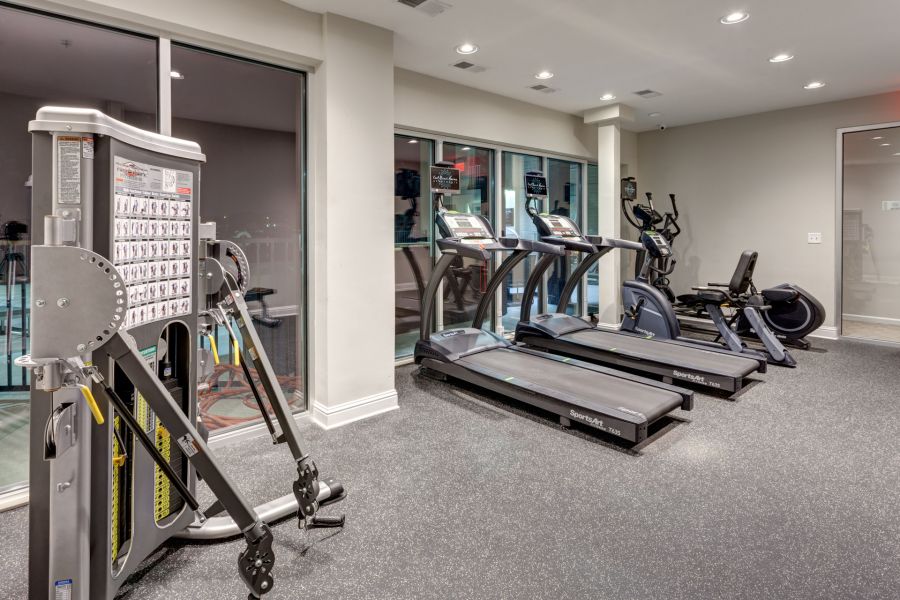 Modern gym with treadmills, elliptical machines, and a weight machine beside large windows at night.