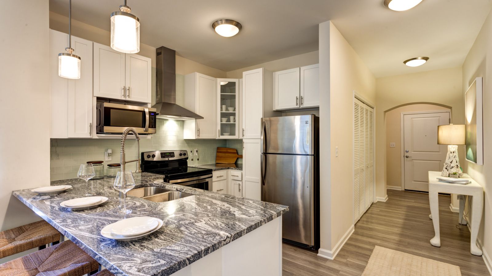 Modern kitchen and living area with white cabinets, stainless steel appliances, and a large island. Cozy seating area with a sofa and rug in the background. Bright and inviting atmosphere.