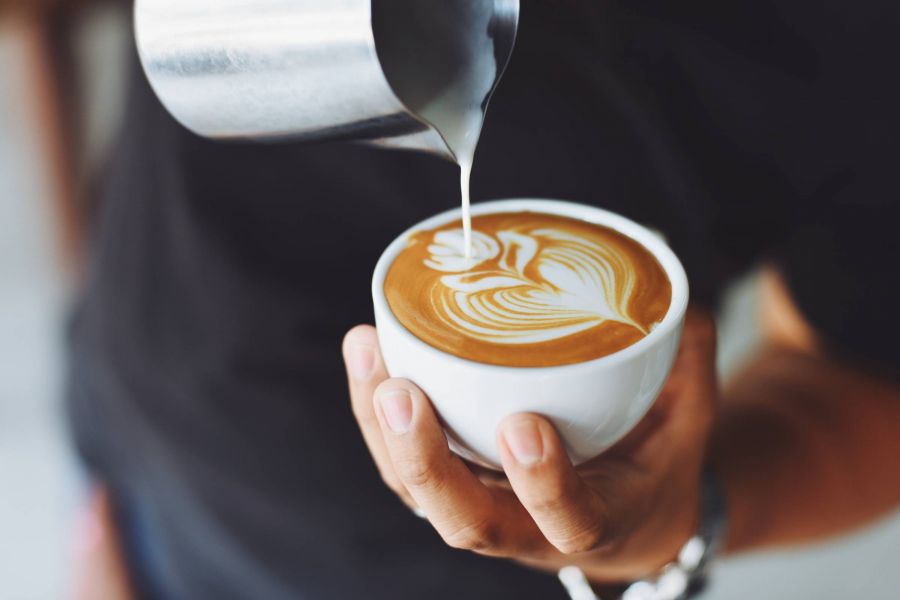 Hand holding a cup of coffee with latte art as milk is being poured into it.