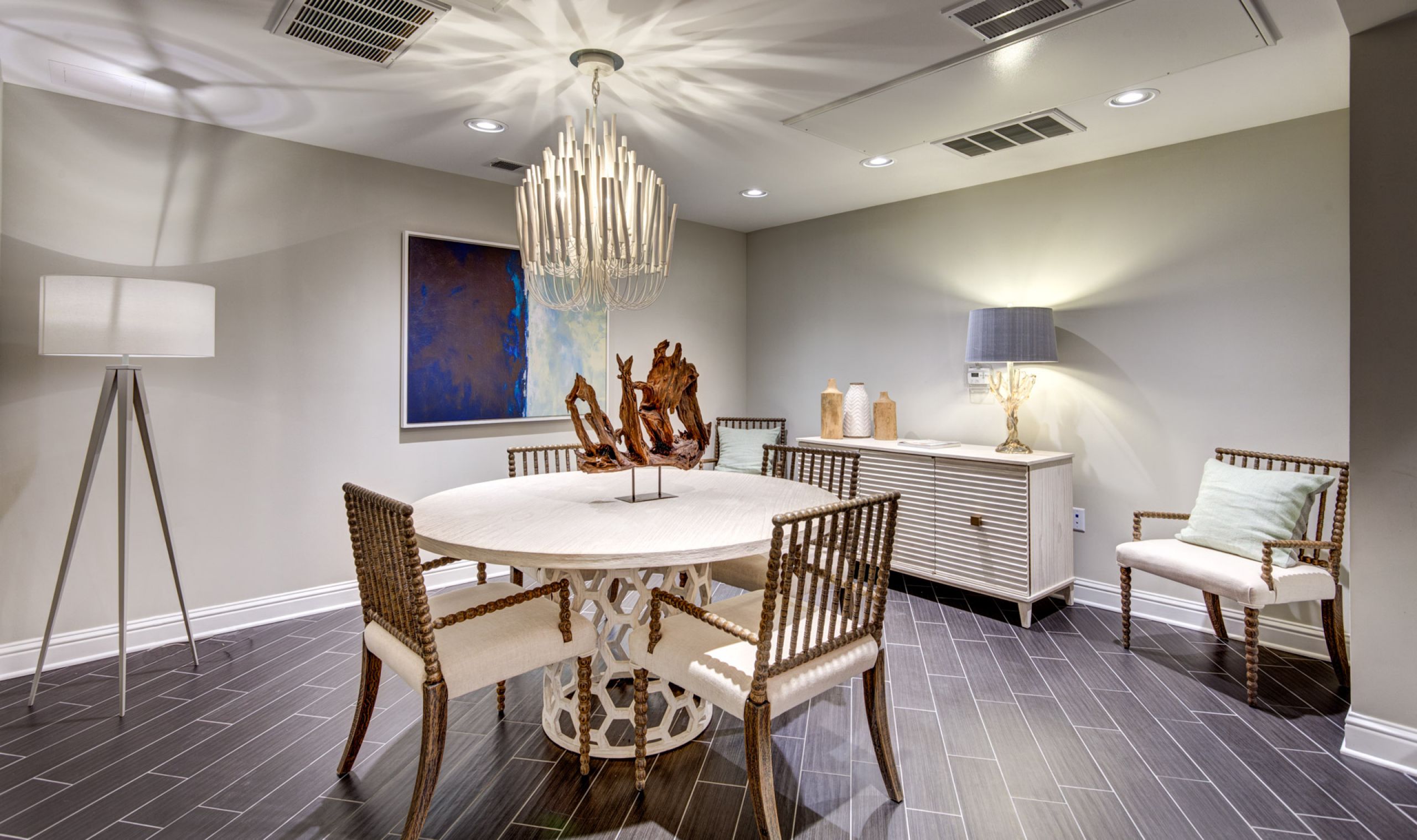 Modern dining room with round table, wicker chairs, chandelier, sideboard, and contemporary decor.